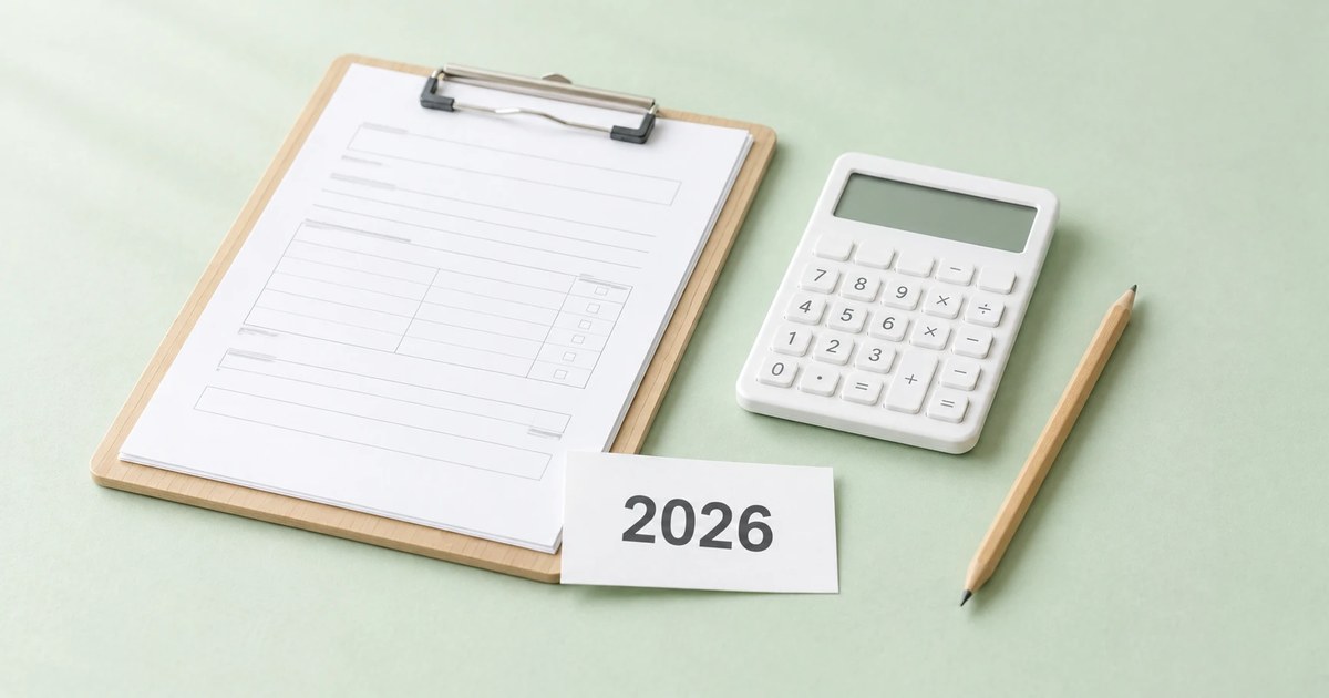 淡いミントグリーンの紙の上に、書類を挟んだクリップボード、電卓、鉛筆と、「2026」と書かれたカード