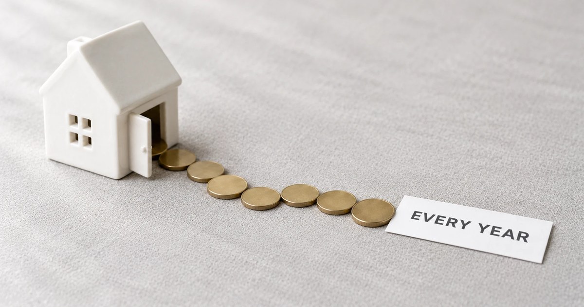 グレーの布の上で、白い家の置物の開いた玄関から硬貨が一列に出て行き、その先に「EVERY YEAR」のカード